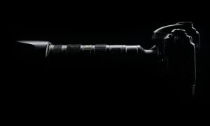 Silhouette of a modern camera with lens against a dark black backdrop.